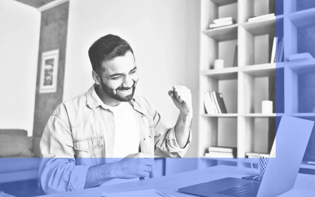 A man celebrates good news in front of a laptop