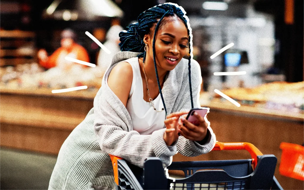 A person pushing a cart in a grocery store using their smartphone device