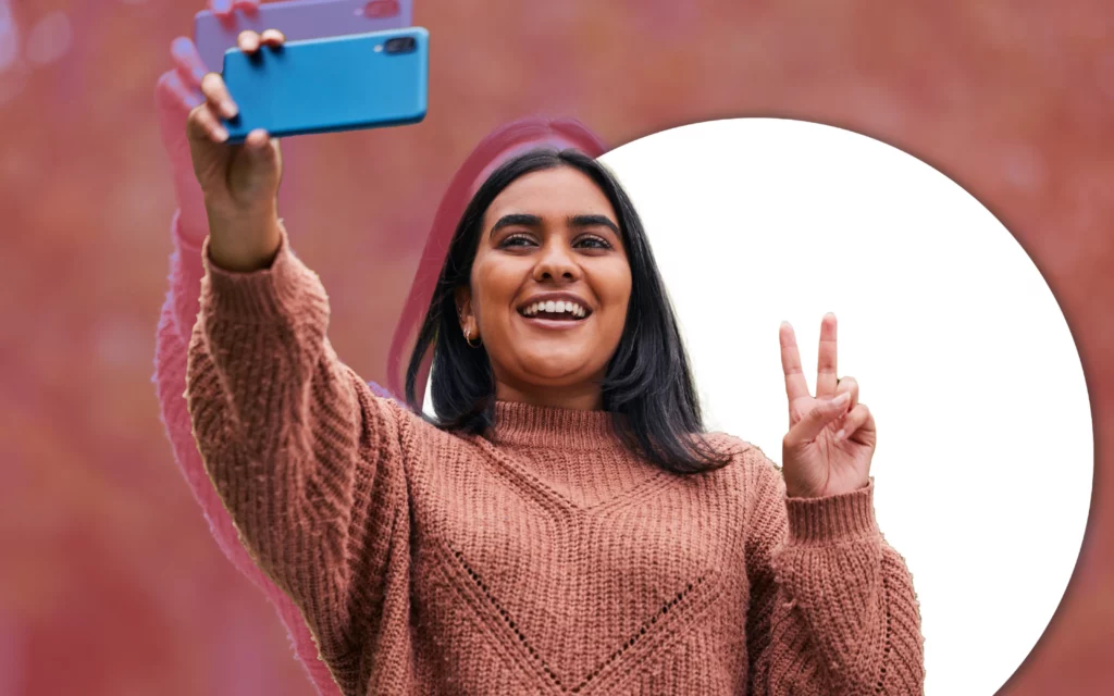 A young lady takes a selfie with a smartphone while giving the peace sign
