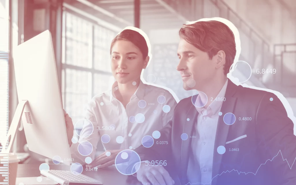 A man and woman look intently at a desktop computer screen that references the stock market