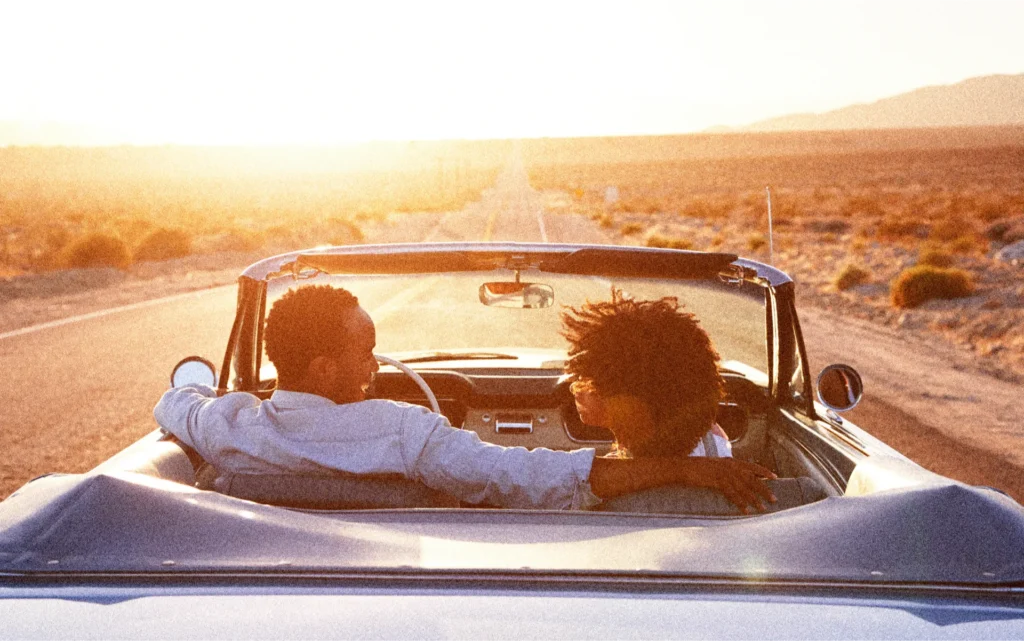 Two people drive off into the sunset in a convertible car