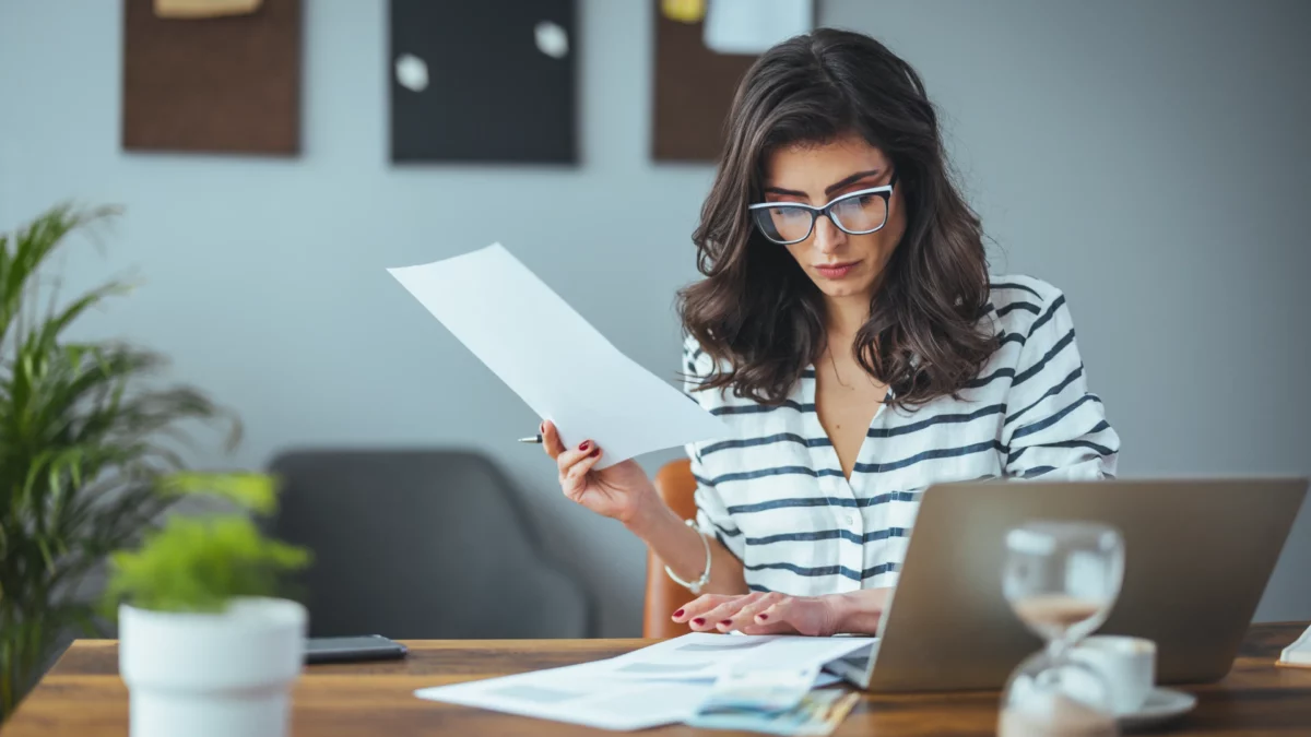 middle-aged-woman-with-glasses-sitting-down-at-a-desk-doing-taxes-with-a-laptop